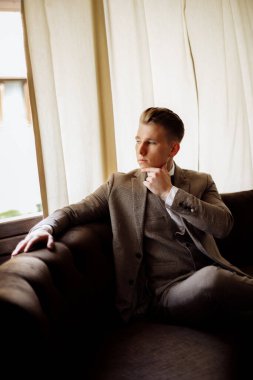 Bir adamın portresi. Gri takım elbiseli, beyaz gömlekli ve papyonlu damat kahverengi deri koltukta oturuyor. Koltukta oturan takım elbiseli damat. Yüksek kalite fotoğraf