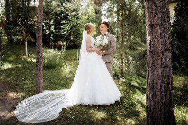 Baharın arka planında güneşli yeşil ormanda lüks bir gelin ve damat. Birbirine aşık bir çift. Yüksek kalite fotoğraf