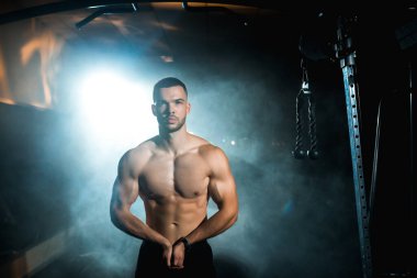 Atletik bir adamın portresi tişörtsüz duruyor ve elleri kalçasında başka yere bakıyor. Yüksek kalite fotoğraf