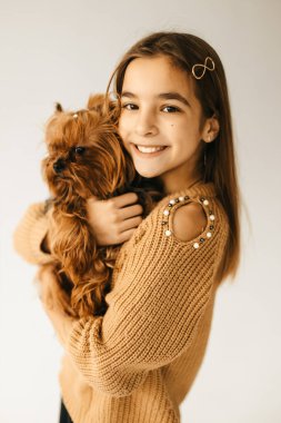 Küçük güzel bir kızın portresi beyaz bir arka planda elinde bir köpekle kıs kıs kıs gülüyor, uysal küçük kahverengi bir köpek. Yüksek kalite fotoğraf
