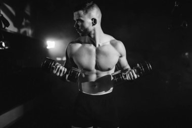 Sporcu bir adam spor salonunda kol pazılarının kasları üzerinde egzersiz yapar. Siyah-beyaz fotoğraf. Yüksek kalite fotoğraf