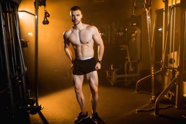 Karanlık bir spor salonunda, sıcak bir zeminde poz veren kaslı bir sporcu, sporcu portresi. Yüksek kalite fotoğraf
