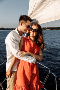 Yatın kenarında birbirine aşık bir çift el ele tutuşur, sevgi gösterir, güçlü kucaklaşmalar, mavi deniz, beyaz yelkenli yat. Sevgililer günün kutlu olsun. Yüksek kalite fotoğraf