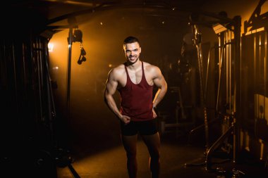 Kaslı adam gülümser ve spor salonunda vücudunun kaslarını gösterir. - Evet. Yüksek kalite fotoğraf