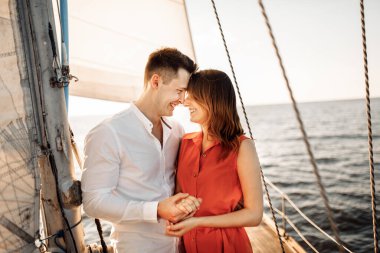 Genç çift denizde yelkenli beyaz bir yatta sarılıp öpüşüyor..