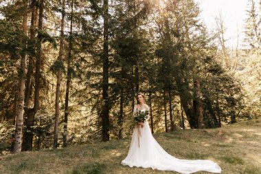 Beyaz elbiseli bir gelin güzel bir düğün buketiyle ormanda duruyor. Yüksek kalite fotoğraf