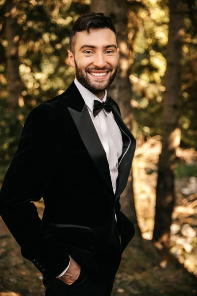 Young smiling man in a black suit with a bow tie. Against the backdrop of nature. High quality photo