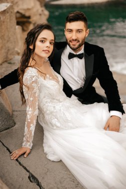 Düğün çifti taştan bir nehrin arka planında oturup sarılıyorlar. Yüksek kalite fotoğraf