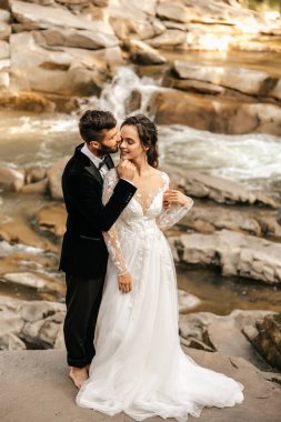 Şelale ve taştan bir nehrin arka planında güzel bir düğün çifti. Yüksek kalite fotoğraf