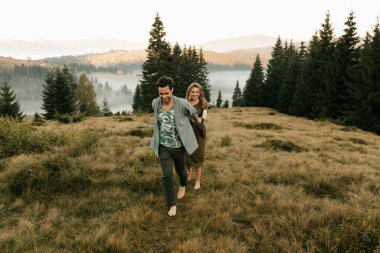 Koyu yeşil elbiseli güzel bir çift doğada dağların arasında yürür. Yüksek kalite fotoğraf