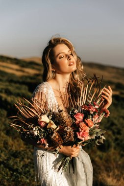 Beyaz bir gelinlik içinde, ellerinde bir buket ile dağların arka planında güzel bir gelin. Yüksek kalite fotoğraf