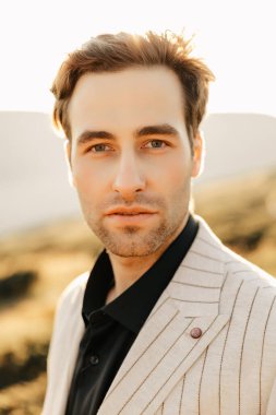 Doğanın arka planına karşı açık renk ceketli yakışıklı bir adamın kendine güveni. Yüksek kalite fotoğraf