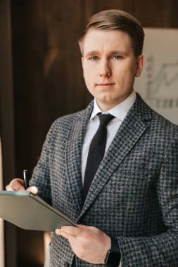 Açık tenli genç, başarılı bir işadamı ve ofis çalışanı elinde belgelerle ofisinde duran bir dosya tutuyor. Ofiste çalışan bir adam, kağıda not alır. Yüksek kalite fotoğraf