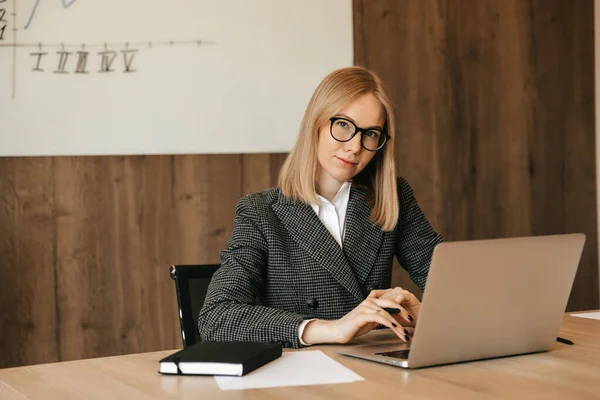 Mutlu genç iş kadını bilgisayar kullanıyor, internette sörf yapıyor, ofis masasında oturuyor, iş yerinde dizüstü bilgisayarına e-posta yazıyor.
