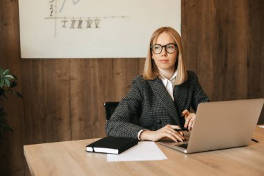 Dizüstü bilgisayar kullanarak çalışan genç ve güzel bir kadın dikkat dağıtıcı bir şekilde pencereden dışarı bakıyor, sorumluluk sahibi bir ofis çalışanı. Yüksek kalite fotoğraf