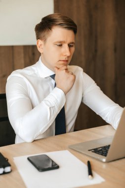 Concentrated man in white shirt working with laptop in office. High quality photo