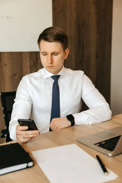 Remote work at the computer. Distracted from work, a man looks at the social network on a smartphone. High quality photo