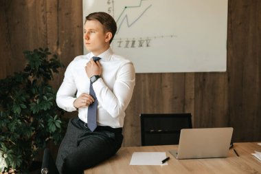 Businessman and office worker man sits at the desk in his office and straightens his tie. High quality photo