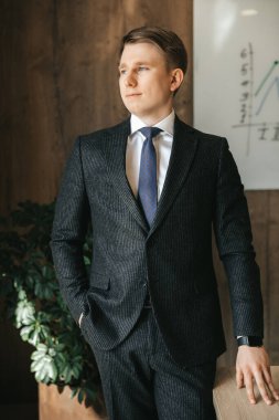 Genç ve başarılı bir iş adamı ofiste klasik bir takım elbisenin içinde duruyor. Yüksek kalite fotoğraf