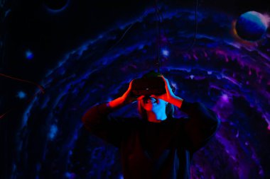 Sanal gerçeklik gözlükleriyle, oyun odasında mavi ve kırmızı ışıkları olan neşeli, genç ve güzel bir kız.