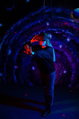 Sanal gerçeklik kaskı kullanan genç bir kız. Uzay arka planında neon kırmızı ve mavi ışıklar. Elini ileri uzat, dur işareti.. 