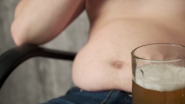 Den feta mannen äter chips och dricker öl. Handen kliar ölmagen. Ölmage från skadlig mat. Dålig mat, frosseri. Närbild. — Stockvideo