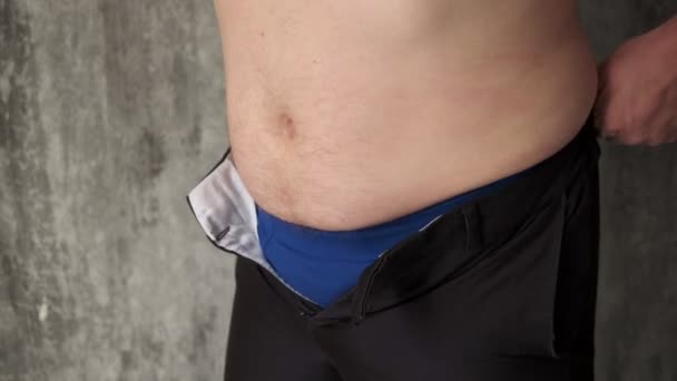 Gros homme ne peut pas boutonner votre pantalon en raison de prévenir l'estomac.Sauter et essayer de boutonner les pantalons.Gros ventre prévenir boutonnement.Obésité chez les hommes.Sur un fond gris. gros plan — Video