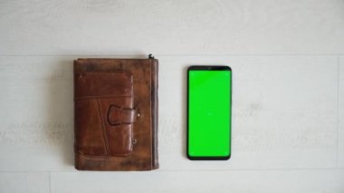 Masanın üzerinde yeşil ekranlı telefon, üstten defter ve çanta görünümü, akıllı telefon kromakey ekran kopyalama alanı 