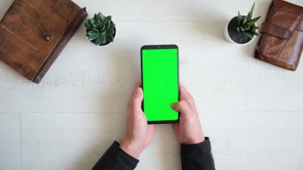 Téléphone avec écran vert sur la table avec ordinateur portable et sac à main vue du haut, espace de copie d'écran chromatique smartphone — Video