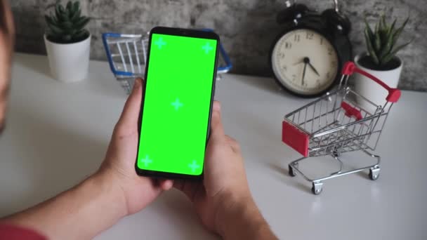 Mesa com cestas de compras close-up telefone celular em mãos com tela verde. desliza na tela do chromakey smartphones em close-up. vídeo ready-made para inserir e digitar conteúdo online — Vídeo de Stock