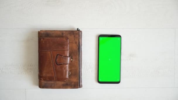 Telefoon met groen scherm op de tafel met notebook en portemonnee bekijken van boven, smartphone chromakey scherm kopieerruimte — Stockvideo