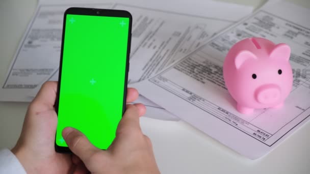 녹색 화면과 돼지 은행 지불 영수증과 흰색 배경 위에 세금 문서가 있습니다. 스마트폰 크로마키는 다른 방향으로 스냅 합니다. 복사 공간 — 비디오