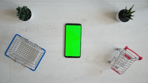 Um telefone com uma tela cromakey verde e um carrinho de compras em um fundo branco. Vista do topo do smartphone — Vídeo de Stock