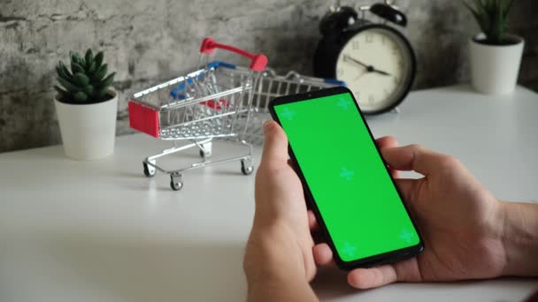 Mesa com cestas de compras close-up telefone celular em mãos com tela verde. desliza na tela do chromakey smartphones em close-up. vídeo ready-made para inserir e digitar conteúdo online — Vídeo de Stock