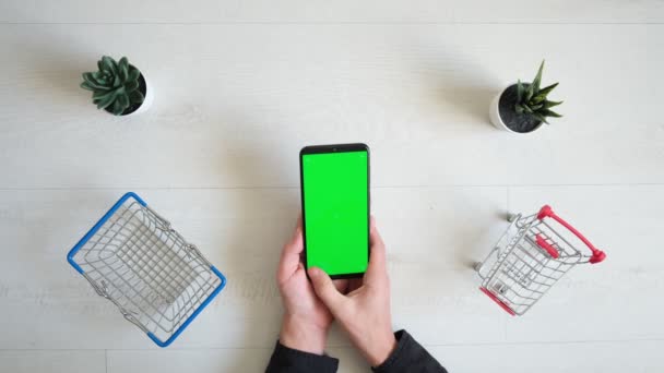 Un telefono con schermo cromakey verde e carrello della spesa su sfondo bianco. vista dall'alto dello smartphone nelle mani di un primo piano — Video Stock