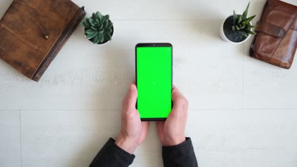 Telefon se zelenou obrazovkou na stole s notebookem a kabelkou pohled shora, smartphone chromakey obrazovka kopírovací prostor — Stock video