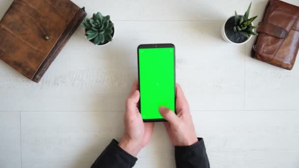 Teléfono con pantalla verde en la mesa con portátil y vista al bolso desde la parte superior, espacio de copia de pantalla cromakey smartphone — Vídeos de Stock