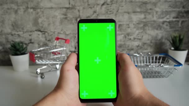 Tisch mit Einkaufskörben in Großaufnahme Handy in den Händen mit grünem Bildschirm. Wischen auf dem Smartphone-Bildschirm in Großaufnahme. Ready-made-Video zum Einfügen und Keying von Inhalten online — Stockvideo