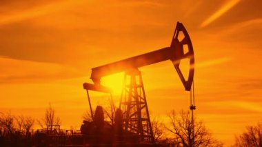 Bir yağ makinesinin silueti. Günbatımının arka planında petrol pompalama platformu. Yüksek kalite 4k görüntü
