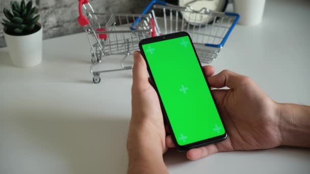 Mesa com cestas de compras close-up telefone celular em mãos com tela verde. desliza na tela do chromakey smartphones em close-up. vídeo ready-made para inserir e digitar conteúdo online — Vídeo de Stock