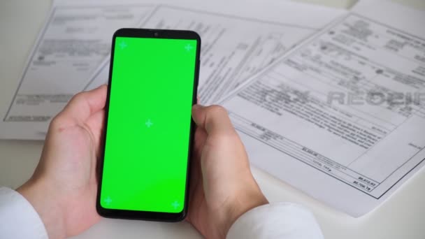 Telefon z zielonym ekranem i wpływy z płatności, dokumenty podatkowe na białym tle góry Widok. smartphone chromakey przesuwa się w różnych kierunkach. przestrzeń kopiowania — Wideo stockowe