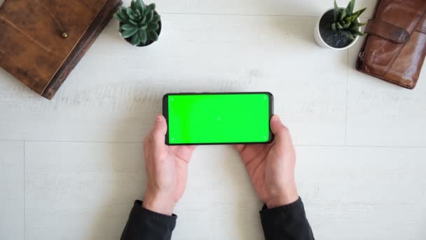 Telefono con schermo verde sul tavolo con notebook e vista borsa dall'alto, spazio di copia dello schermo cromakey smartphone Filmato Stock
