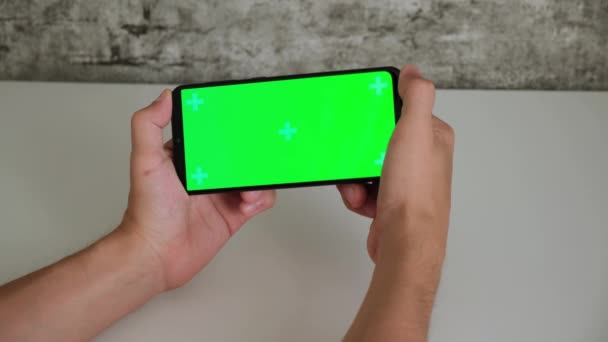 Ένας άνδρας σε ένα λευκό γραφείο κάθεται με ένα κινητό τηλέφωνο στα χέρια του με μια πράσινη οθόνη. σαρώνει και πατάει στην οθόνη chromakey smartphones σε κοντινό πλάνο. έτοιμο βίντεο για εισαγωγή και πληκτρολόγηση Βίντεο Αρχείου