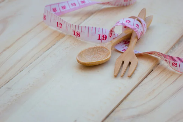 Wooden kitchen wooden spoon and fork on wooden background with measuring tape — Stock Photo, Image