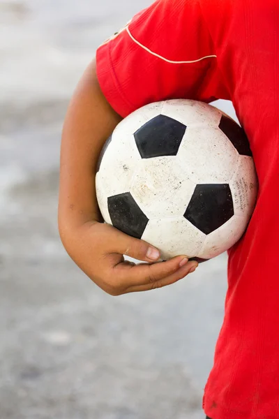 boy with red t-shirt holding dirty black white football or socce