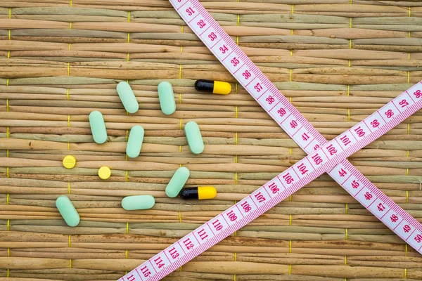 Pilules et ruban à mesurer croisé sur tapis traditionnel. régime alimentaire ou perdre — Photo