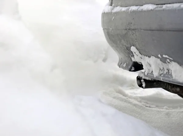 Exhaust pipe of gray car fumes, emits gases into  snow and contaminates the environment. Focus on pipe.