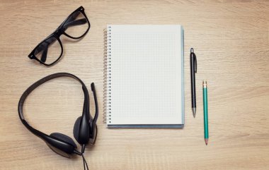 Online eğitim. Kulaklık, gözlük, not defteri, kalem ve kalemle en iyi öğrenci masası. Dinlemek ve sesli kitapların notlarını almak.