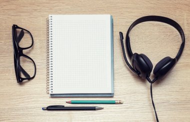 Online eğitim. Kulaklık, gözlük, not defteri, kalem ve kalemle en iyi öğrenci masası. Dinlemek ve sesli kitapların notlarını almak.