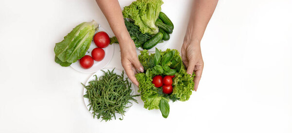 Close-up of female hands lays a salad of fresh tomatoes and cucumbers, arugula leaves and lettuce on the table. Diet vegetable food.